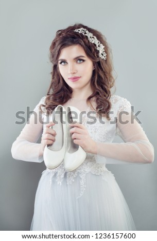 Beautiful bride woman holding white bridal shoes. Fiancee in wedding dress