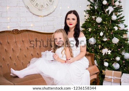 Christmas and family concept - happy mother and little daughter in living room with Christmas tree and gifts