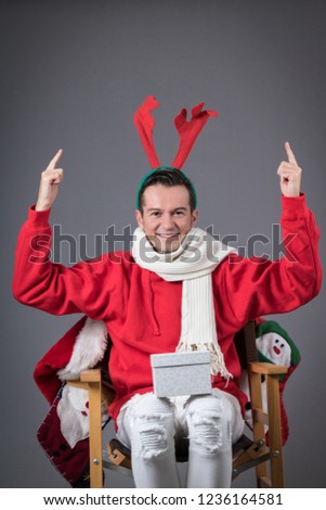 Happy man with reindeer antlers pointing above his head while holding gift box in his lap. Copy space. 