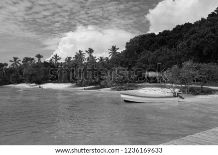 picture of small fisherman boat moored near the beach of atlantic ocean shore in the samana bay. Cayo Levantado island is covered with palm trees. Sky is cloudy but the sun is harsh.