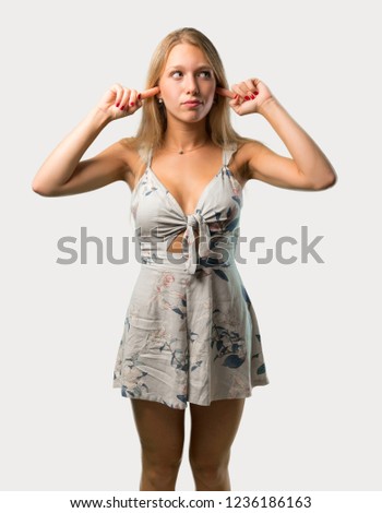 Young blonde woman covering both ears with hands on grey background