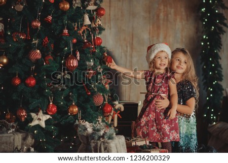 Merry Christmas and Happy Holiday! Two cute little children girls sisters open magic gift box on Christmas. Cozy  room with New year decoration and Christmas tree 