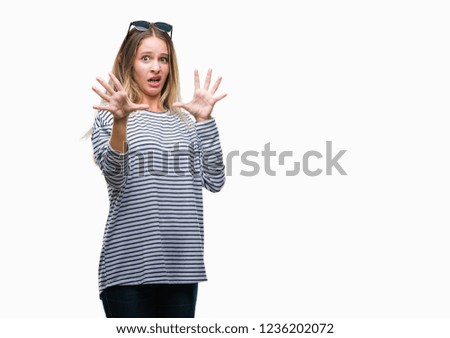 Young beautiful blonde woman wearing sunglasses over isolated background afraid and terrified with fear expression stop gesture with hands, shouting in shock. Panic concept.