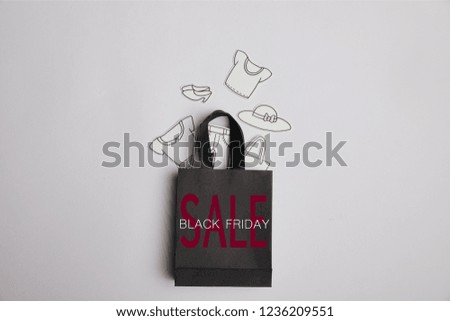top view of black shopping bag with black friday sale inscription and paper clothes on grey background