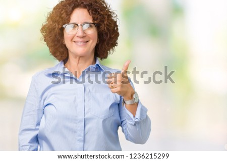 Beautiful middle ager senior businees woman wearing glasses over isolated background doing happy thumbs up gesture with hand. Approving expression looking at the camera showing success.