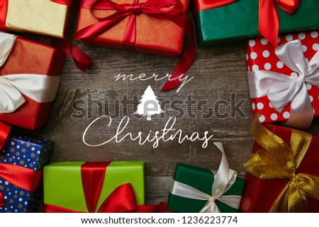 flat lay with presents wrapped in different wrapping papers with ribbons on wooden surface with "merry christmas" lettering