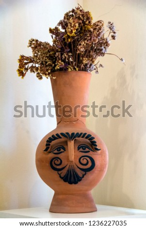 Old clay vase with human face drawing on it with dried flowers