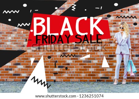 stylish young woman with shopping bags using smartphone while standing in front of brick wall, black friday sale banner