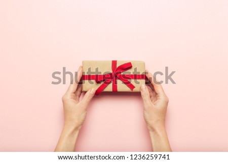 Female hands holding a gift box on a pink background with a question mark. Surprise concept, waiting for a gift for the holidays, birthday, christmas, wedding. Flat lay, top view