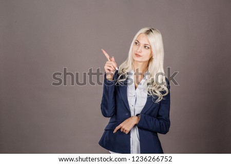 Young smiling woman shows something on grey background. lifestyle and people concept.