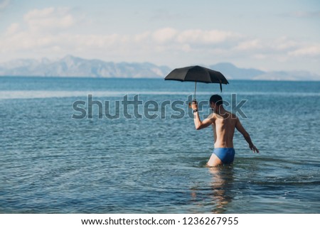 Young man swims with an umbrella in the sea