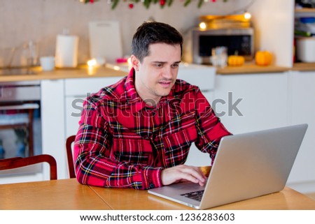 White middle age man in red t-shirt looking for Holiday sale-out in Internet via laptop computer in Christmas time.