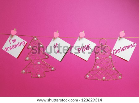 "I'm dreaming of a Pink Christmas" message written on hanging white signs with gold festive holiday ornaments pegs on a line bunting against a pretty pink background.