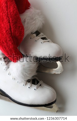 White skates for winter sports, sharp blades with tine, fluffy and red hat of Santa Claus. White background. Top view.