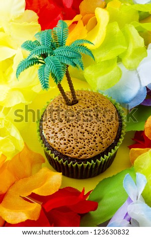 Close-up shot of cupcake with plastic coconut tree miniature surrounded by colorful flowers.
