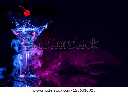 cherry falling into a martini cocktail splash on blue and purple smoky background