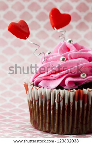 Hearts sticking out of icing on a cupcake on a pink surface.