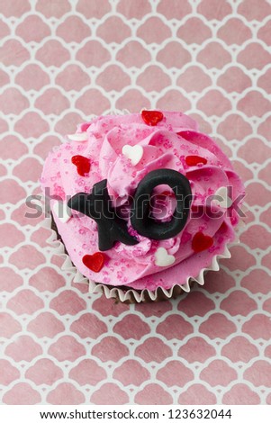 Close-up top view of strawberry cupcake with heart shape and alphabets.