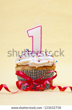 Close-up image of a cupcake with number 1 candle and streamer tied around cupcake over yellow background.