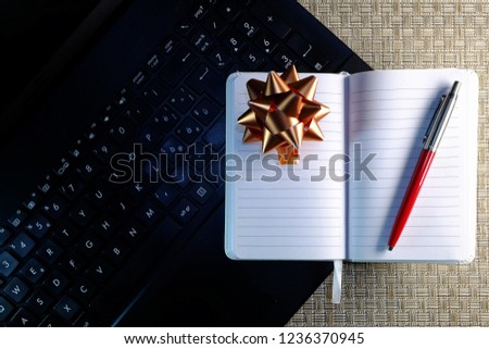 Desk with a backdrop reminiscent of the straw effect on which a laptop computer rests, a white diary and an elegant ballpoint pen. Christmas decoration of gold color.