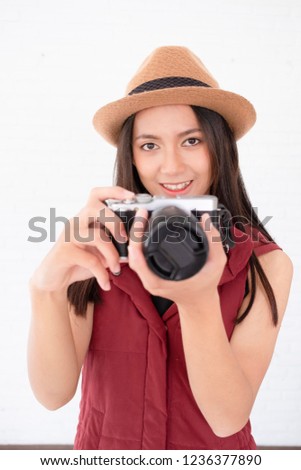 Portrait young girl holding camera in hand with white block wall.