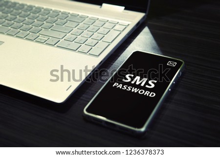 Table with open laptop and black-screened smartphone with white written words SMS password on its display. Concept of linking the work of computer and mobile via sms password entering. One time code Royalty-Free Stock Photo #1236378373