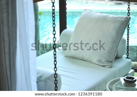 The outdoor porch swing sitting is located at the corner of the terrace outside room with swimming pool background, this area for reading, relaxing or drinking tea.