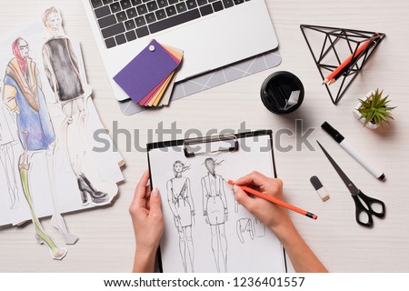 office desk with laptop, art supplies and cropped view of designer working on sketches, flat lay