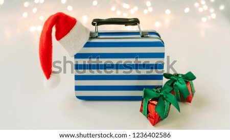travel case with a santa claus hat and gifts around. White background with blured lights