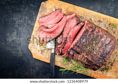 Traditional barbecue dry aged sliced roast beef steak with herbs as top view on an old cutting board with copy space left Royalty-Free Stock Photo #1236408979