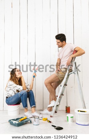 Portrait of young couple man and woman using ladder while painting wall and making renovation indoor