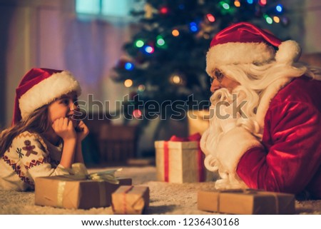 Little charming girl with happy Santa Claus are lying on the floor in beautiful house decorated for Christmas. Waiting for New Year together.