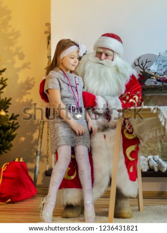 Santa Claus in the interior is talking to a girl against the background of a Christmas tree.