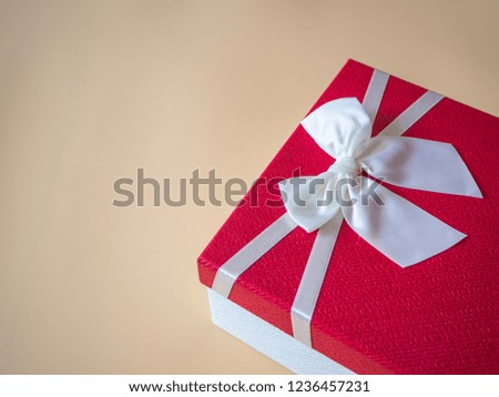 Gift red box and white bow on brown light color background with empty space. Space for text.