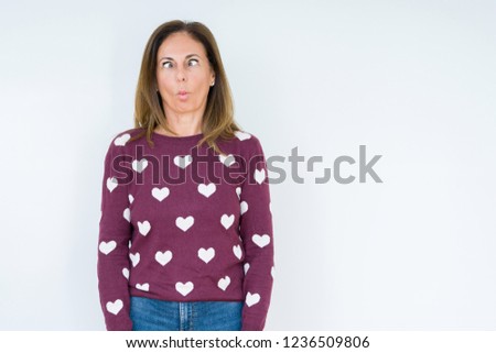Beautiful middle age woman wearing heart sweater over isolated background making fish face with lips, crazy and comical gesture. Funny expression.