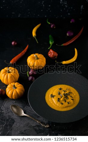 Pumpkin orange cream soup with pumpkin seeds in black plate. Dark photo. Smakk pumpkin, chilly papper around.