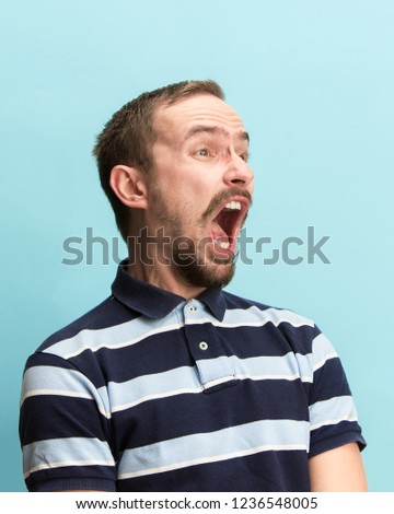 The surprised and astonished young man screaming with open mouth isolated on blue background. concept of shock face emotion