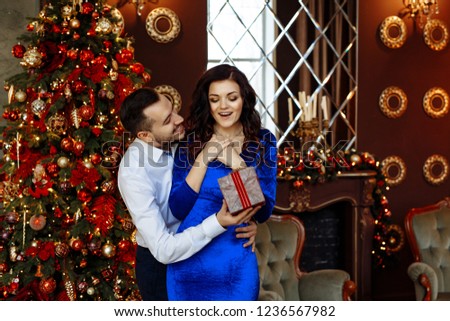 A couple in love celebrates Christmas at home. a man gives a woman a surprise gift on the background of Christmas tree