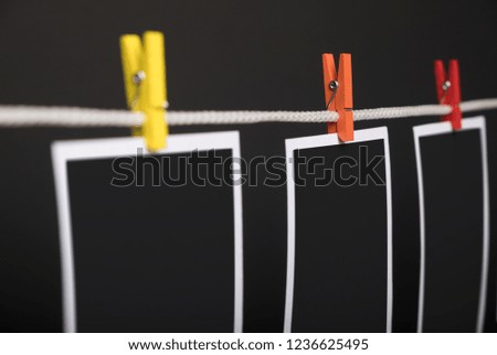 Three empty instant photo cards with red clothespins hanging on rope against black wall