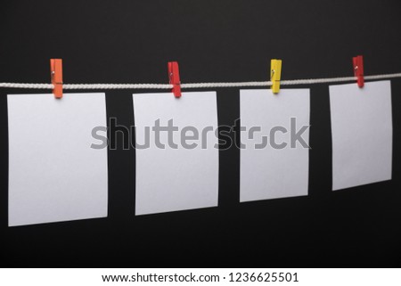 Empty white paper cards with colored clothespins hanging on rope against black wall