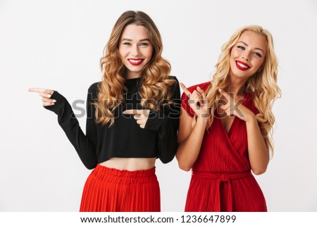 Image of emotional young two girls friends gossiping isolated over white wall dressed in black and red clothes pointing to copyspace.