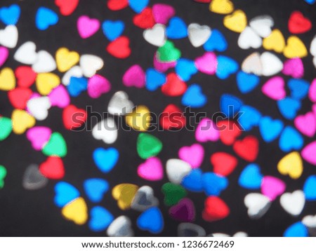 Colorful shiny hearts lie on a black background. Hearts are blurry. Background image.