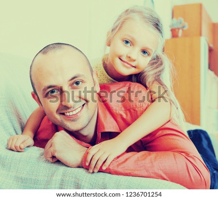 Portrait of happy middle-aged dad with cute little girl hugging and smiling indoors

