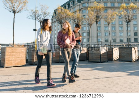 Outdoor portrait of teenage students with backpacks walking and talking. City background, golden hour.