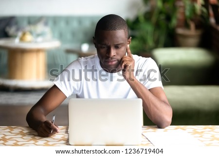 Focused African American man using laptop in cafe, serious black student looking at computer screen, thinking about online project, task, reading e-book, news, journalist writing, think about article Royalty-Free Stock Photo #1236719404