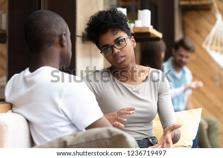 Focused African American woman talking with man in cafe, girlfriend discussing relationships with boyfriend, explaining, gesticulating, friends having serious conversation, sitting together on couch Royalty-Free Stock Photo #1236719497