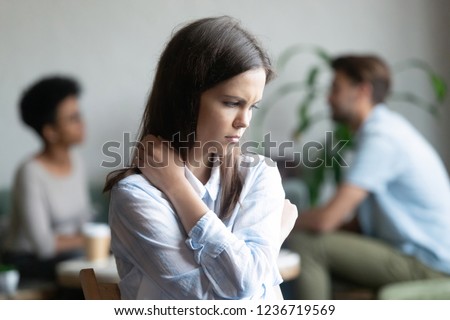 Upset young woman sitting alone in cafe offended at diverse couple friends, depressed female feeling outsider, depressed, jealous, suffering from low self-esteem, discrimination, hugging herself Royalty-Free Stock Photo #1236719569