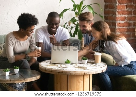 Happy smiling diverse friends using laptop together in cafe, watching funny video online, comedy movie during lunch in coffee house, multiracial people having fun together, free time activities Royalty-Free Stock Photo #1236719575