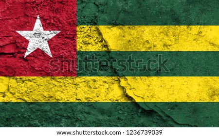 Flag of Togo close up painted on a cracked wall, concept of armed actions and conflicts in the world