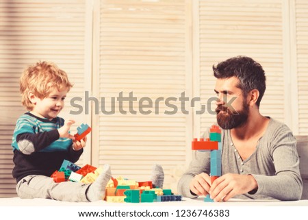 Man with beard and boy play together on wooden wall background. Dad and kid build of plastic blocks. Father and son with busy faces create colorful robot of toy bricks. Family and childhood concept